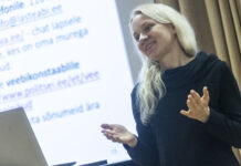 Vihakõnedest internetis – tapa ta oma headusega! Naisterahvas rõõmsameelse ilmega loengut pidamas, Taamal tekst ekraanil, esiplaanil vasemas nurgas sülearvuti.