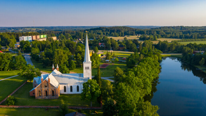 Esiplaanil Kambja Püha Martini kirik ja Kambja järv. Taamal aleviku korruselamud ja Köstrimäed.