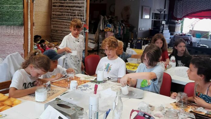 Lapsed istuvad käsitöötoas ja kaunistavad klaaspurke küünlaümbristeks.