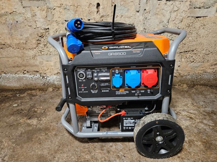 Oranž ja must GrupeL GR6500 elektrigeneraator siniste ja punaste pistikupesadega, paigutatud siseruumi betoonpõrandale.