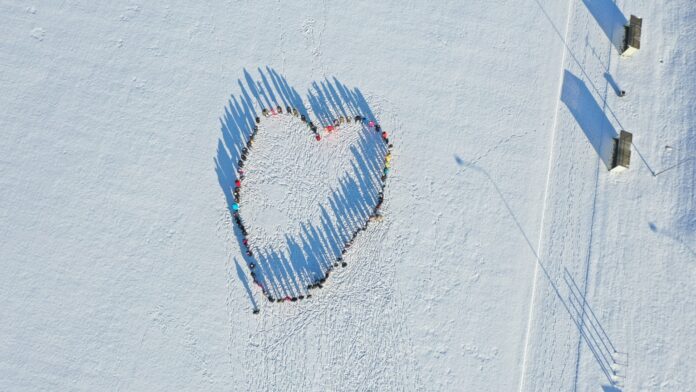 Droonifoto lumisel väljakul seisvatest inimestest, kes moodustavad südamekuju