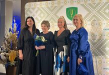 Eesti raamatu aasta Tõrvandi Raamatuklubis Neli naist poseerivad tunnustussündmusel foto jaoks Kambja valla sümboolikaga taustaseina ees. Ühel neist on käes lillekimp.