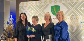 Eesti raamatu aasta Tõrvandi Raamatuklubis Neli naist poseerivad tunnustussündmusel foto jaoks Kambja valla sümboolikaga taustaseina ees. Ühel neist on käes lillekimp.