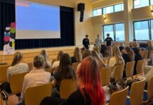 Kambja valla noorte karjääripäev kinnitas, et oma tee kujuneb tegutsedes Auditooriumis toimub esitlus, kus kolm noormeest tutvustavad lava ees seistes õppesuundi ja võimalusi. Ekraanil kuvatakse slaid „Õppekavad“, publikuks on peamiselt noored, kes kuulavad tähelepanelikult. Ruum on valgusküllane, suurte akendega ning istutakse ridades toolidel. Vasakul on näha stend kirjaga „LEEN“. Õhkkond on informatiivne ja suunatud hariduslike valikute tutvustamisele.