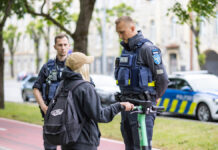 Elektritõukerataste kontroll näitab, et laste liikluskäitumine on murettekitav Linnatänaval peatavad kaks politseinikku elektritõukerattaga sõitva noore inimese. Vestlus toimub rahulikult: üks ametnikest seisab sõitja ees ja selgitab midagi, teine jälgib olukorda veidi eemal. Taustal on park, puud ja ajaloolised hooned ning tee ääres politseiauto. Tõukeratas on roheline ning sõitjal on seljas tume riietus ja seljakott. Stseen viitab liiklusjärelevalvele või ohutuskontrollile linnakeskkonnas.