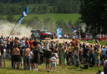 WRC Delfi Rally Estonial saab näha maailma parimaid ja noori Eesti tippsõitjaid Esiplaanil seisab tihe rahvahulk, kes jälgib kruusateel kihutavat ralliautot. Paljud inimesed hoiavad käes Eesti lippe ja meeskonnalippe ning filmivad või pildistavad sündmust telefonidega. Keskel sõidab värviline ralliauto suure tolmupilve saatel kurvi läbides. Rada on piiratud turvavõrkude ja reklaambänneritega. Taustal on näha rohelised põllud ja metsaservad, mis loovad suvise Lõuna-Eesti maastiku meeleolu