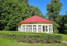 Kohvik Rotund on taas avatud Väike ajalooline kohvikuhoone punase katuse ja suurte akendega keset hooldatud parki. Hoonet ümbritsevad madalad hekid ning kõrged puud loovad rohelise ja suvise meeleolu. Päikeseline ilm ja sinine taevas.