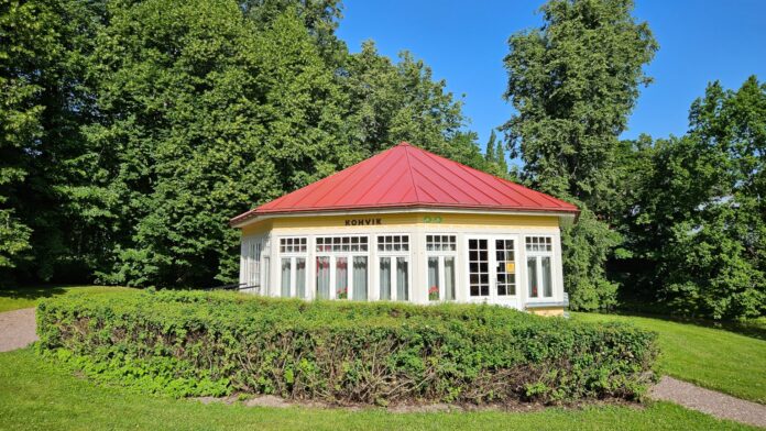 322_5_rotund Väike ajalooline kohvikuhoone punase katuse ja suurte akendega keset hooldatud parki. Hoonet ümbritsevad madalad hekid ning kõrged puud loovad rohelise ja suvise meeleolu. Päikeseline ilm ja sinine taevas.